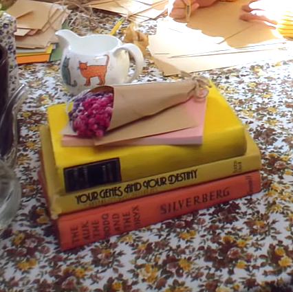 A stack of three books with flowers on top. There is a teacup in the background.